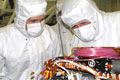 Link to Mars Program - A photograph of two engineers dressed in clean room suites looking at a piece of flight hardware.